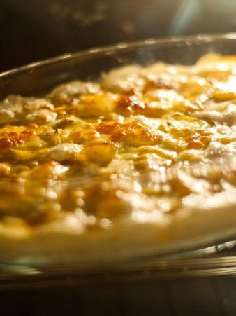 Rezept Foto vom gebutterten Kartoffelgratin. Das Foto zeigt eine Bratröhre, indem der Kartoffelgratin langsam goldbraun wird. Eine schöne Käse Kruste bildet sich langsam.