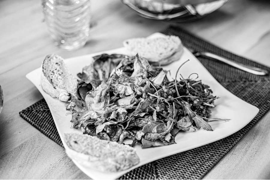 Rezept Foto Himbeer Balsamico Dressing. Foto in Schwarz Weiss. Der Himbeer Balsamico Dressing und Kürbiskernöl angemacht Salat angerichtet auf einem großen Teller mit ein paar Brotscheiben an den Rädnern.