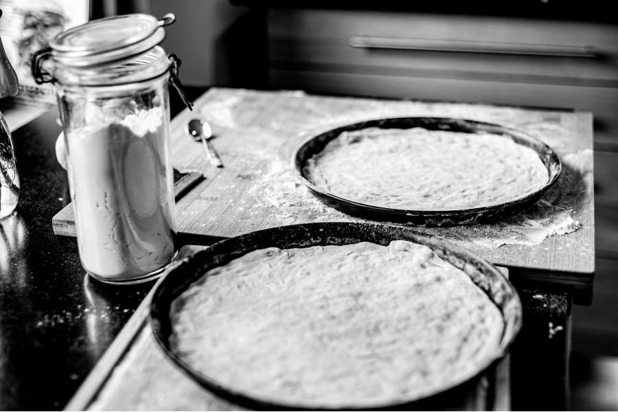 Rezept Foto Holzofen Pizza Komplettanleitung. Foto in Schwarz-Weiss. Zwei Pizzableche stehen nebeneinander, sie sind mit dem fertigen Pizzateig ausgelegt und warten darauf mit Sugo bestrichen zu werden.