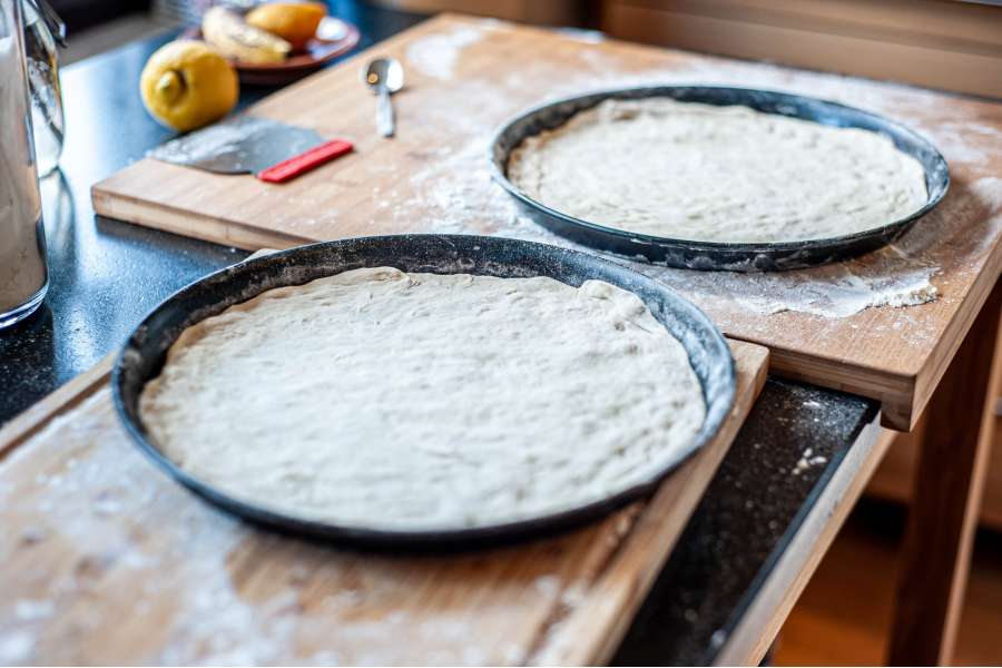 Rezept Foto Holzofen Pizza Komplettanleitung. Foto in Farbe. Zwei Pizzableche stehen nebeneinander, sie sind mit dem fertigen Pizzateig ausgelegt und warten darauf mit Sugo bestrichen zu werden.