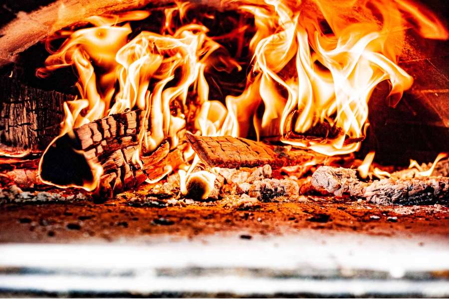 Rezept Foto Holzofen Pizza Komplettanleitung. Brasselndes Feuer im Holzofen sorgt beim Nachschüren für ordentlich Hitze.