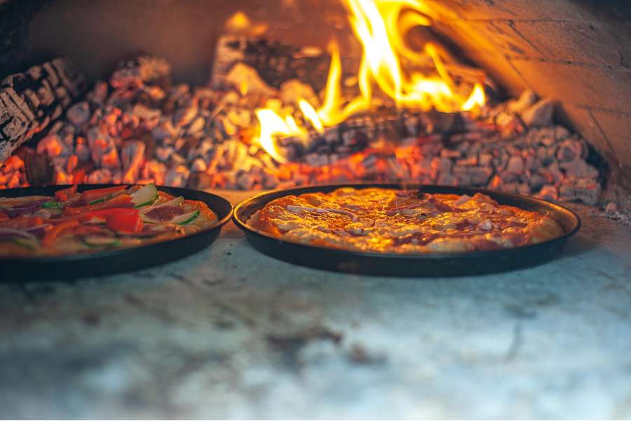 Rezept Foto Holzofen Pizza Komplettanleitung. Die Pizza bruzzelt gerade im kräftig brennenden Holzofen.