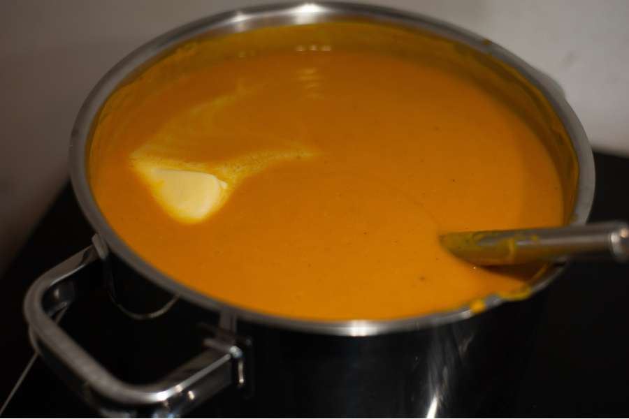 Rezept Foto Detailaufnahme Kürbis Creme Suppe mit einem Stück Butter im Kochtopf