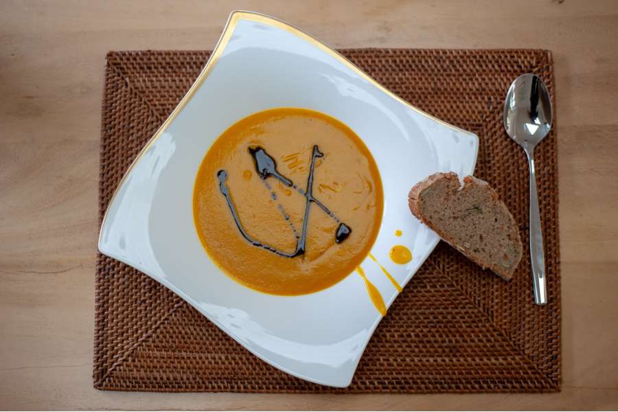 Rezept Foto Kürbis Creme Suppe serviert auf einem Suppenteller mit Kürbiskernöl und frischem Kürbiskernbrot