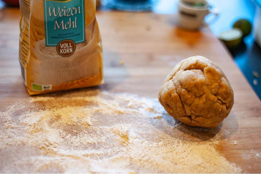 Rezept Foto Lauchzwiebelkuchen backen und genießen. Ein mit Mehl besteubtes Brett und der Mürbeteig des Lauchzwiebelkuchens liegt in einem Ball geformt darauf.