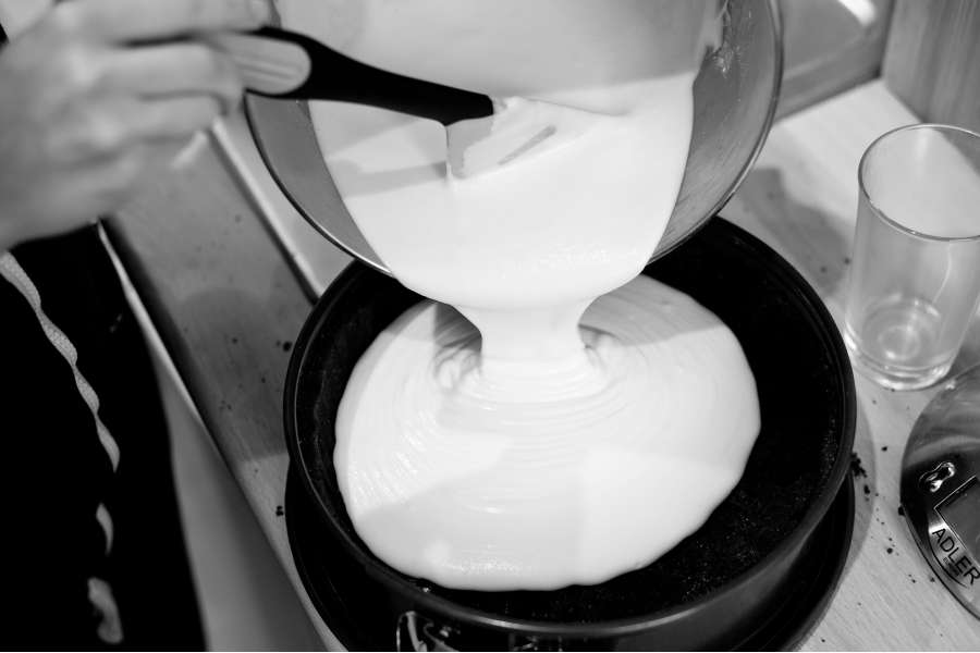 Rezept Foto Russischer Zupfkuchen. Schwarz Weiß Aufnahme: Die Vanillepudding Füllung wird gerade aus der Schüssel auf den Boden gekippt.