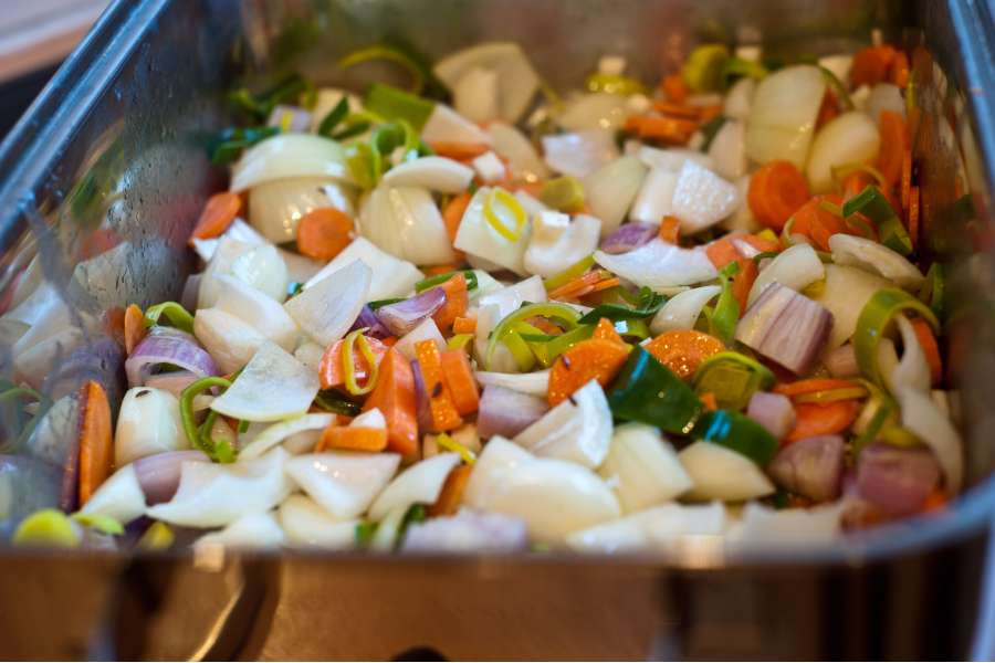 Rezept Foto Bayerischer Schweinebraten in der Kümmelbiersoße. Detailaufnamhe des Bräters mit dem geschnittenen Gemüse wie Zwiebel, Karotten, Lauch und Sellerie.