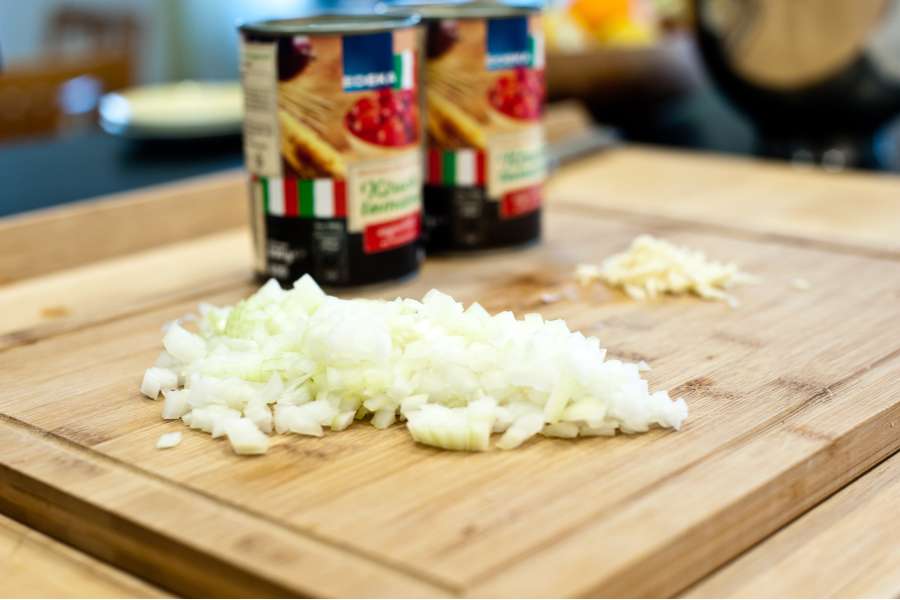 Rezept Foto Grillpizza und Ofenpizza Italien. Schneidebrett mit den gewürfelten Zwiebeln und im Hintergrund stehen die eingelegten Cherrytomaten.