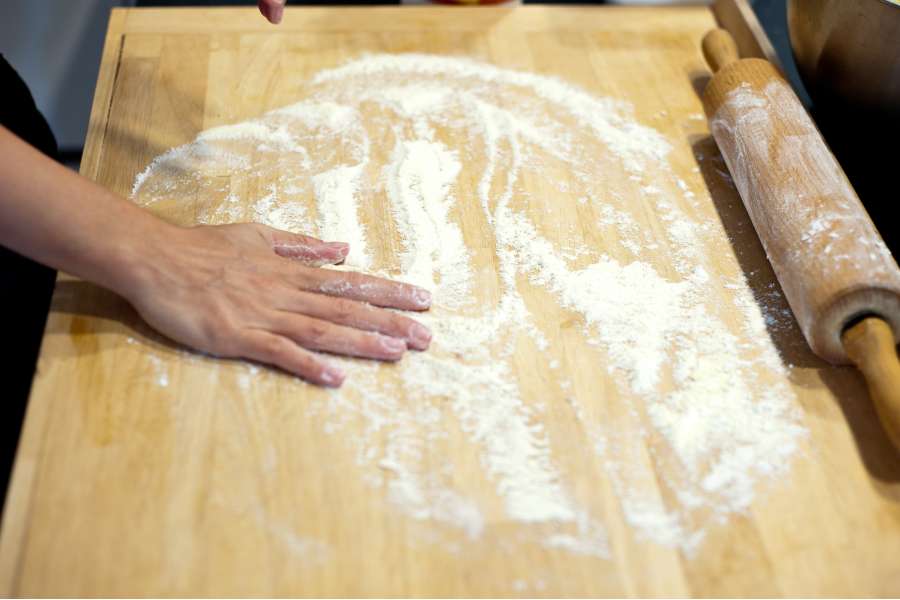 Rezept Foto Grillpizza und Ofenpizza Italien. Katharina bestreut das Küchenbrett für das Ausrollen des Teigs mit Mehl.