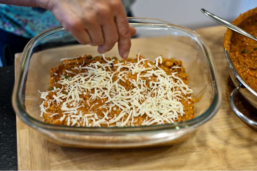 Rezept Foto Lasagne selber machen. Katharina legt auf die Lasagne Platten jeweils eine Schicht Hachfleisch mit Soße und danach Käse auf.