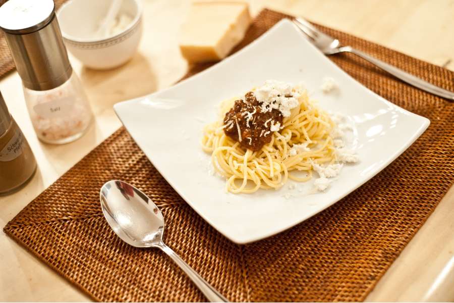 Rezept Foto Rotes Pesto Rosso. Das Rezept angerichtet auf einem Teller. Ein kleiner Haufen Sphaghetti und ein Klecks Rotes Pesto darauf. Als Krönung frischer Parmesan.