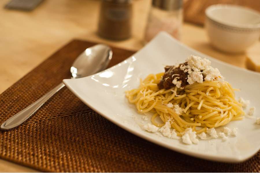 Rezept Foto Rotes Pesto Rosso. Nahaufname des Rezepts, angerichtet auf einem Teller. Ein kleiner Haufen Sphaghetti und ein Klecks Rotes Pesto darauf. Als Krönung frischer Parmesan.