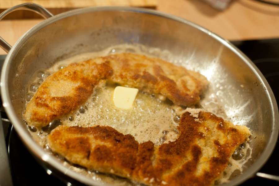 Wiener Schnitzel bereits mit Semmelbrösel paniert in einer Edelstahlpfanne mit viel Butter. Das Schnitzel wird gerade auf mittlerer Temperatur herausgebraten.