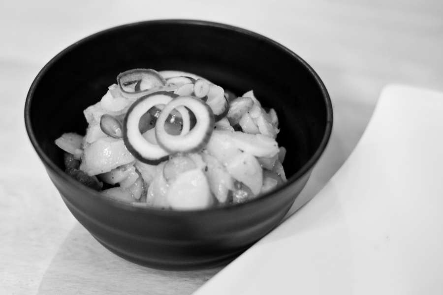 Nahaufnahme vom Kartoffelsalat in einer kleinen Schüssel, garniert mit roten Zwiebeln und ein paar geschnittenen Essiggurken.